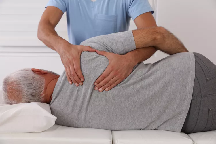 A chiropractic assistant is assisting an older man with improving his strength and activating his back nerves. 