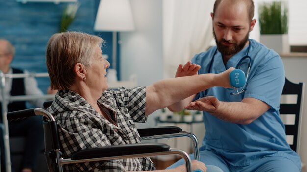 Chiropractic assistant while helping a patient doing physical exercises with dumbbells. 