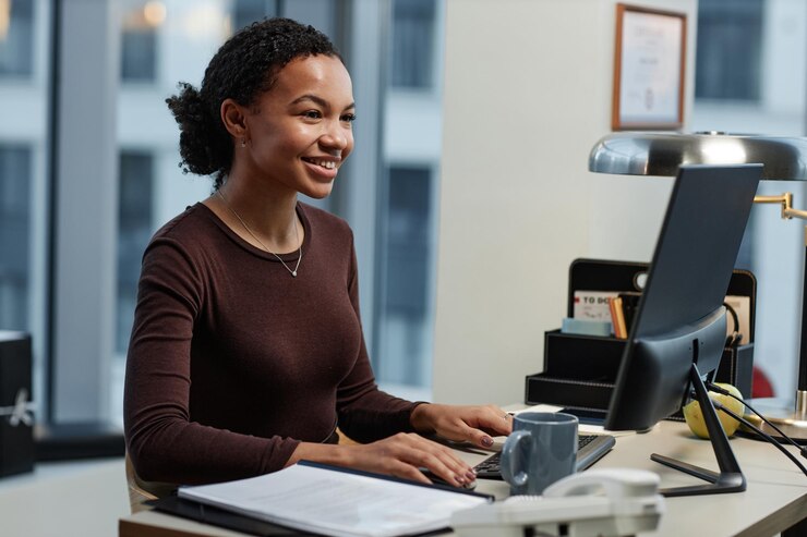 A young data entry clerk using computer desk office smiling enjoying work.