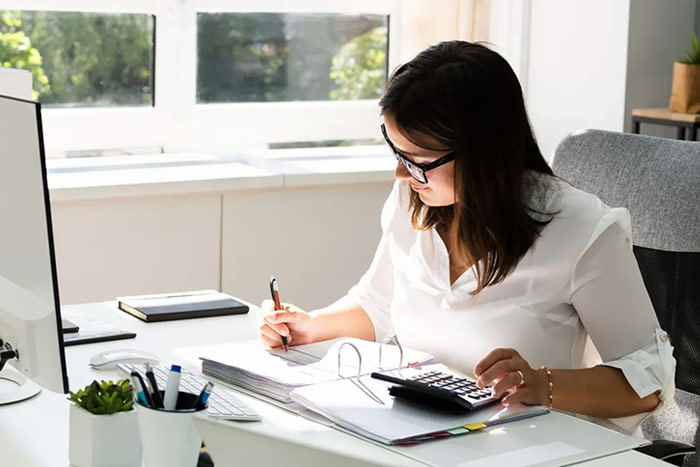 An accountant women monitoring a company's financial activities and checking each ledger using a calculator.
